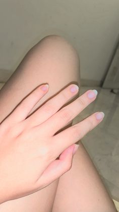 a woman's legs with pink and white manicures on her nails sitting on the floor