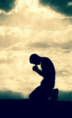 a man kneeling down while looking at his cell phone in front of a cloudy sky