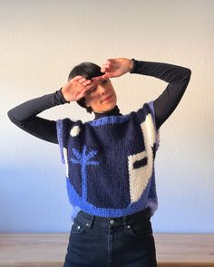 a woman standing in front of a wooden table holding her hands to her head while wearing a blue and white knitted sweater