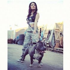 a woman in camo pants holding a dog on a leash