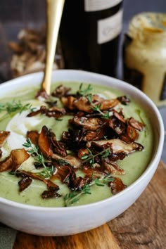 a white bowl filled with broccoli soup and topped with mushrooms next to a bottle of wine