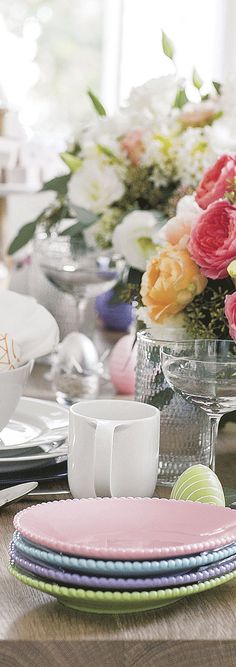 the table is set with plates, cups and vases filled with colorful flowers on it