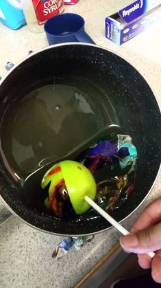 a person holding a spoon in a bowl filled with liquid and plastic candy bar wrappers