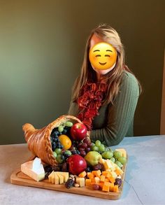 a woman sitting at a table with a tray of fruit and cheese in front of her face