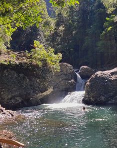 a man is swimming in the water near some large rocks and trees with green leaves on them