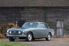 an old grey car parked in front of a barn