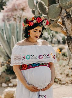 a pregnant woman wearing a flower crown standing in front of a cactus tree with her belly exposed