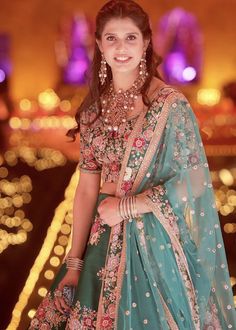 a woman in a blue and green lehenga standing on a stage with lights behind her