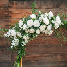 white flowers and greenery are arranged in a gold vase