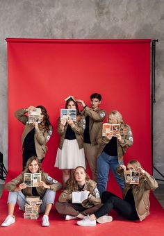 a group of people holding up books in front of a red backdrop with the same image on them