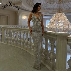 a woman standing in front of a chandelier wearing a long silver dress with sequins on it