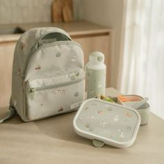 a white backpack sitting on top of a table next to a baby bottle and feeding tray