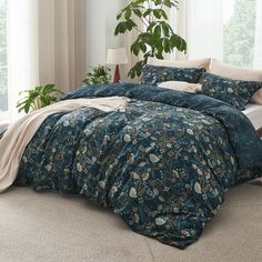 a bed with blue comforter and pillows in front of a large potted plant