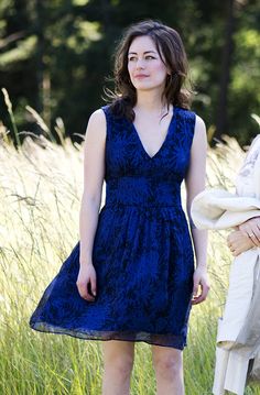 a woman in a blue dress standing next to another woman with her hand on her hip