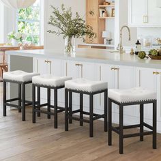 four stools are lined up in front of a kitchen island with white cabinets and wood floors