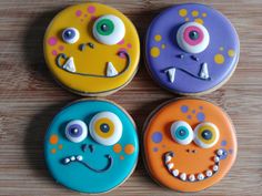 four decorated cookies with eyes and mouths on top of a wooden table next to each other