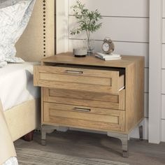 a nightstand with two drawers and a clock on it next to a bed in a bedroom