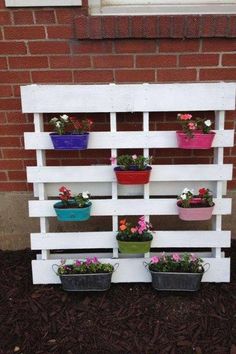 a wooden pallet filled with potted plants on top of dirt next to a brick wall