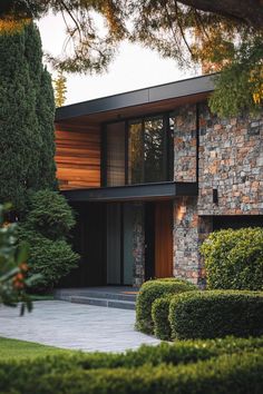 a modern house with stone and wood sidings, surrounded by greenery in the front yard