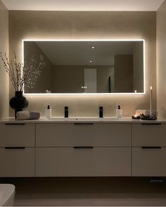 a bathroom vanity with two sinks and a large lighted mirror above it, along with candles on the counter