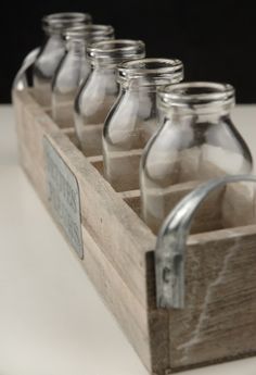 six empty glass jars in a wooden box with metal handles on a white table top