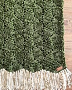 a green crocheted blanket with fringes on it sitting on top of a wooden floor