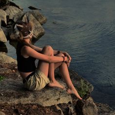 a woman sitting on top of a rock near the water