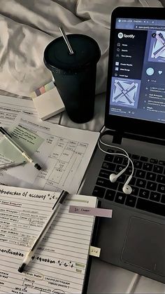 an open laptop computer sitting on top of a bed next to a pile of papers