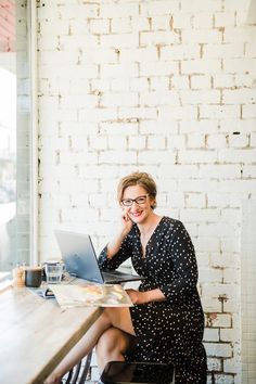 a woman sitting at a table with a laptop in front of her, smiling for the camera