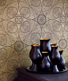 four black vases sitting on top of a table next to a wallpapered wall