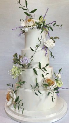 a three tiered cake with flowers and greenery on the top is decorated in white frosting