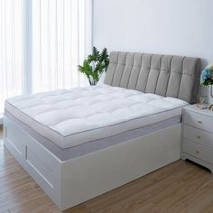 a white bed sitting on top of a wooden floor next to a dresser and window