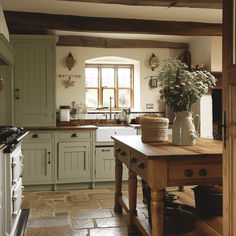 a kitchen with green cabinets and a wooden table in the center, surrounded by stone flooring