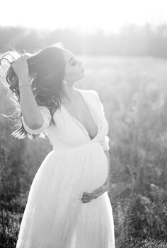 a pregnant woman in a white dress standing in a field with her hands on her head