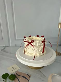 a white cake with red ribbon on top sitting on a table next to a pair of shoes