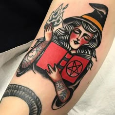 a woman with a book tattoo on her arm is holding a snake and wearing a witches hat