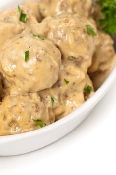 a white bowl filled with meatballs covered in gravy and garnished with parsley