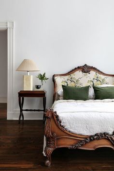 a bedroom with white walls and wood flooring has a large bed, two nightstands, and a lamp on the side table