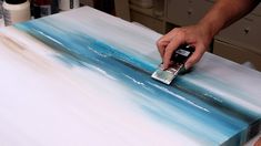 a person is using a brush to paint an ocean scene on a piece of canvas