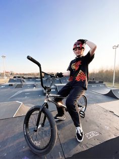 a young man sitting on top of a black bike at a skate park with his arms in the air