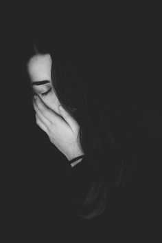 a black and white photo of a woman covering her face with her hands in the dark