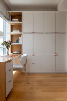 a room with white cupboards and a desk in front of a window that has flowers on it