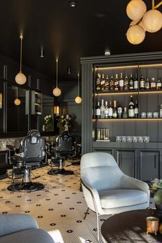 a room with chairs, tables and bottles on the shelves in front of them is lit by lamps