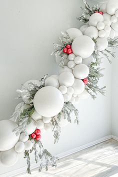 the balloon garland is decorated with white and red balls, greenery, and berries