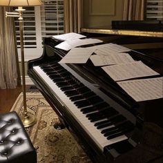 a piano with sheet music sitting on top of it in front of a lamp and window