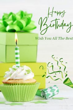 a cupcake with white frosting and a lit candle on it next to green boxes