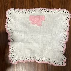 a crocheted blanket with a pink bow on the front and white back, sitting on a wooden floor