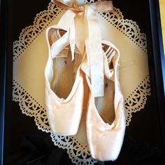 two pairs of ballet shoes sitting in a black box on a doily with lace