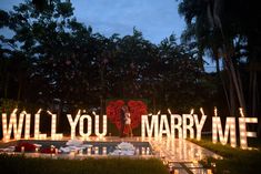 a bride and groom standing in front of candles that spell out will you marry me?