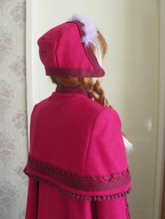 the back of a woman's pink coat with a white feather on it, standing in front of a wall